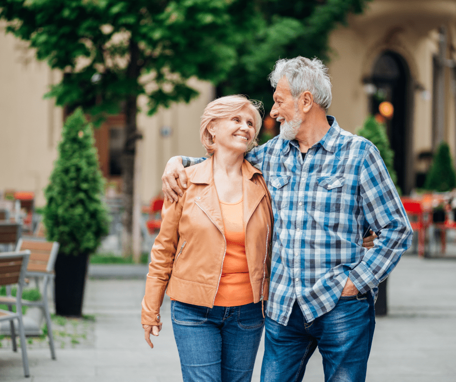Senior couple on a walk outside smiling at eachother, the mans arm is around the woman.
